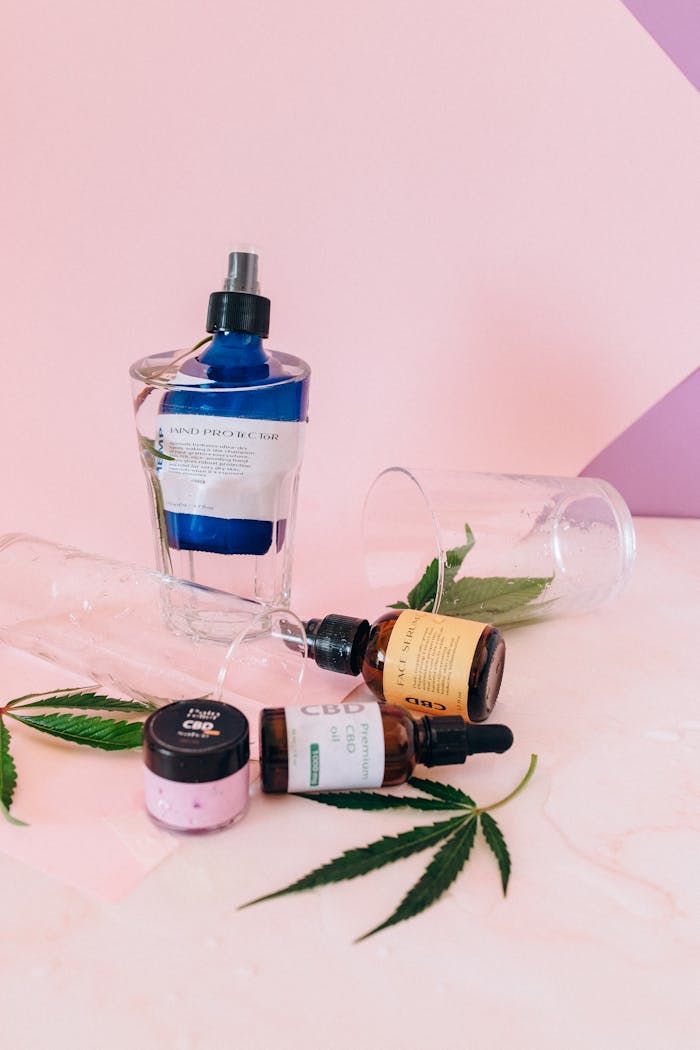 Variety of CBD products with bottles and leaves on a pink backdrop.